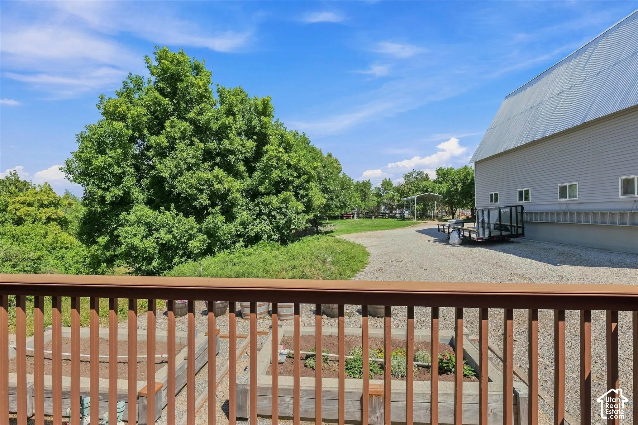 Elevated deck with wood railing, raised garden beds, expabarnnsive gravel area, and a  with multiple windows