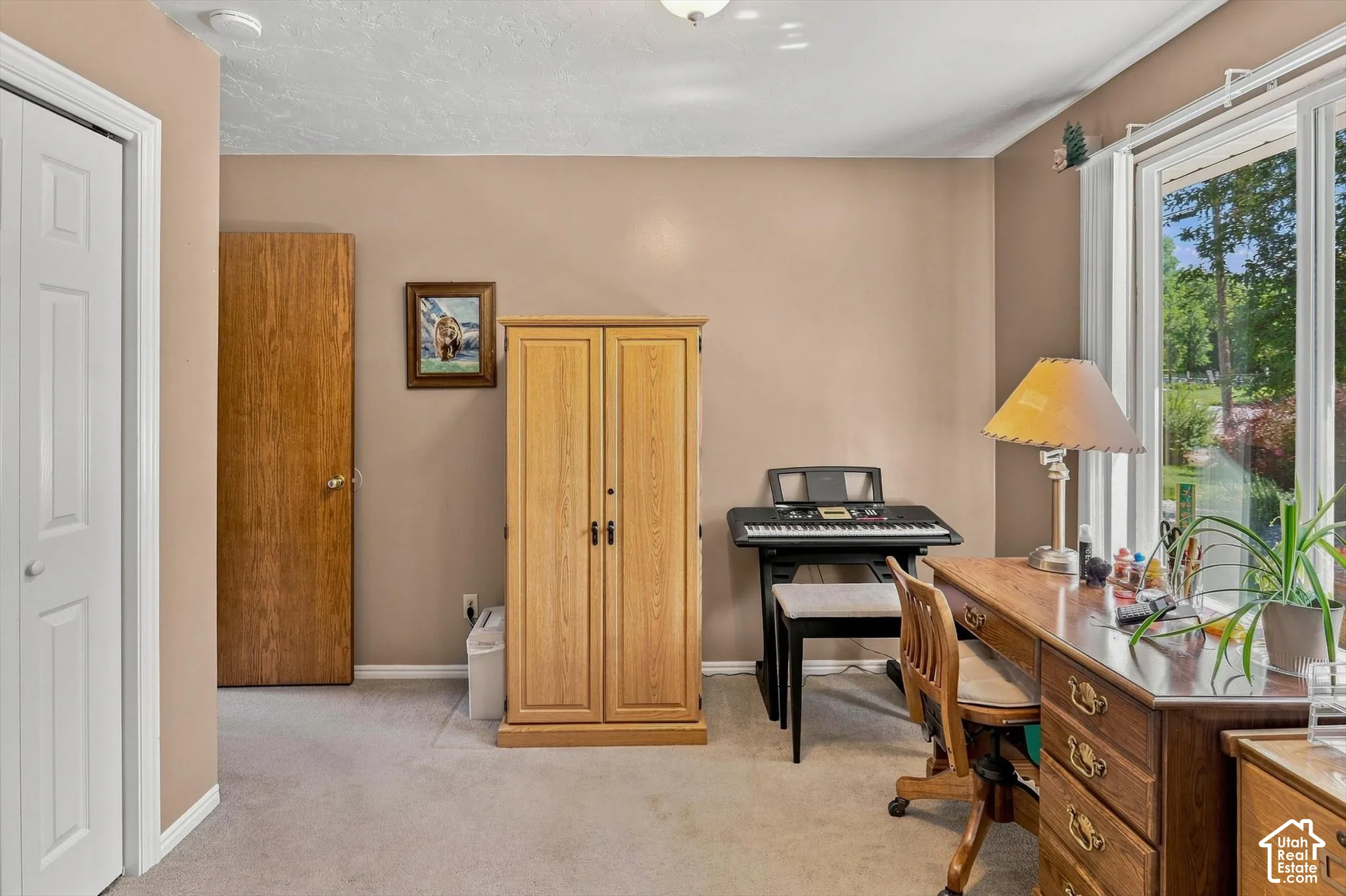 Carpeted office or third bedroom just off the entry door with a white bi-fold door, a solid wood door, and a large window