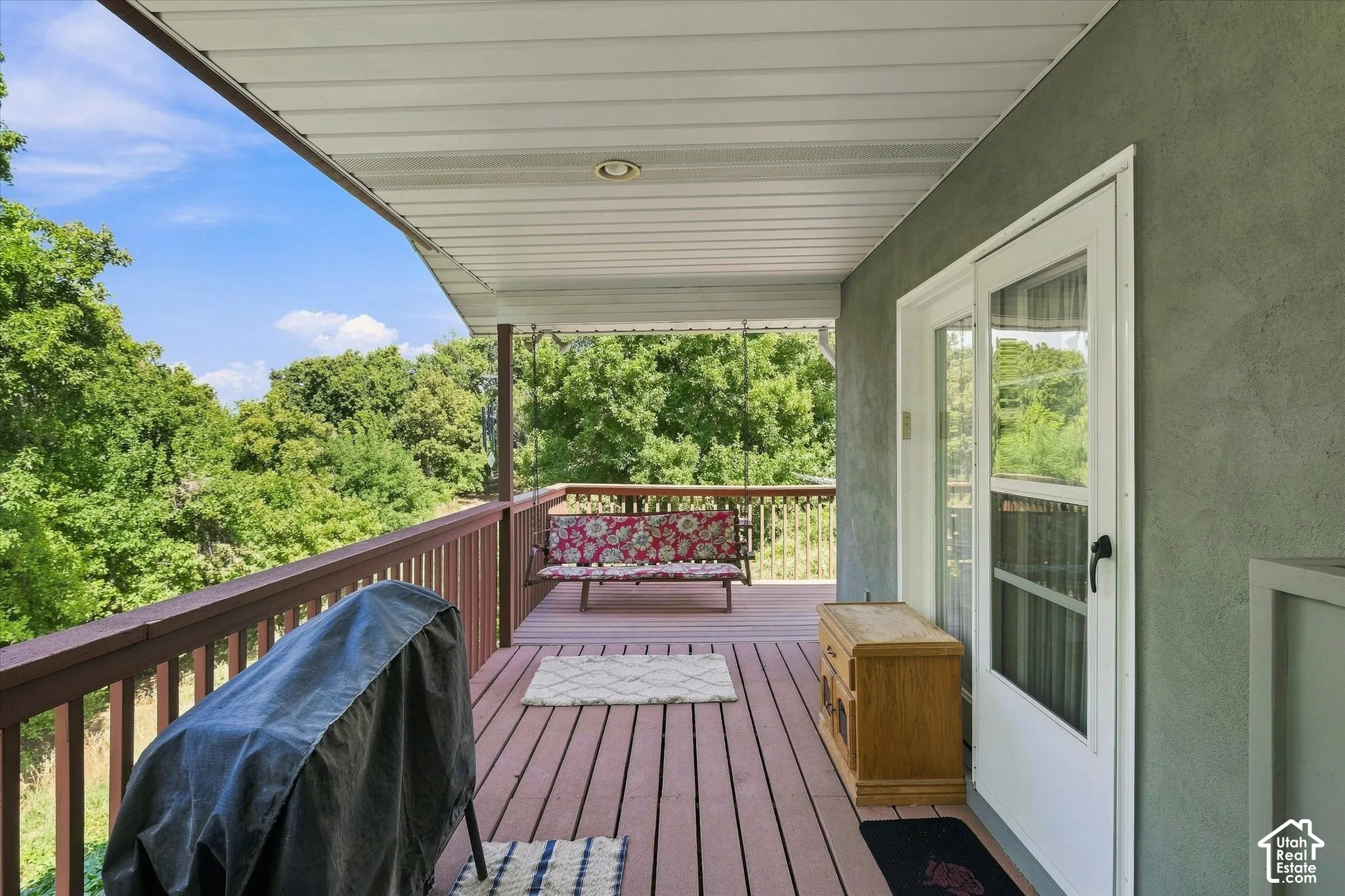 Covered outdoor deck with wood-finish flooring, wood railings, and a sliding glass door leading into the dining room