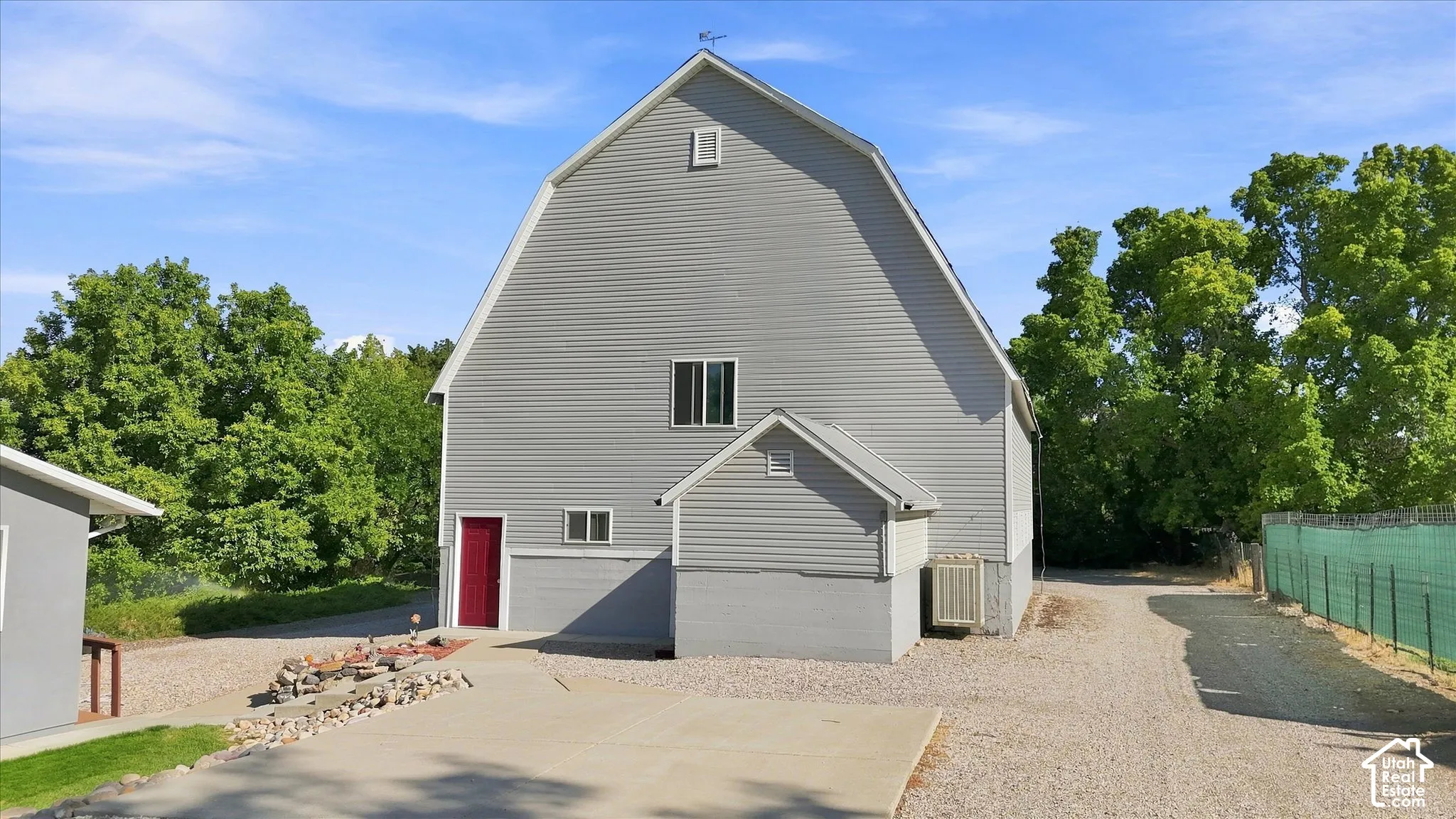Gambrel roof structure with horizontal siding, a red entry door, and a gravel driveway. It's a great barn!