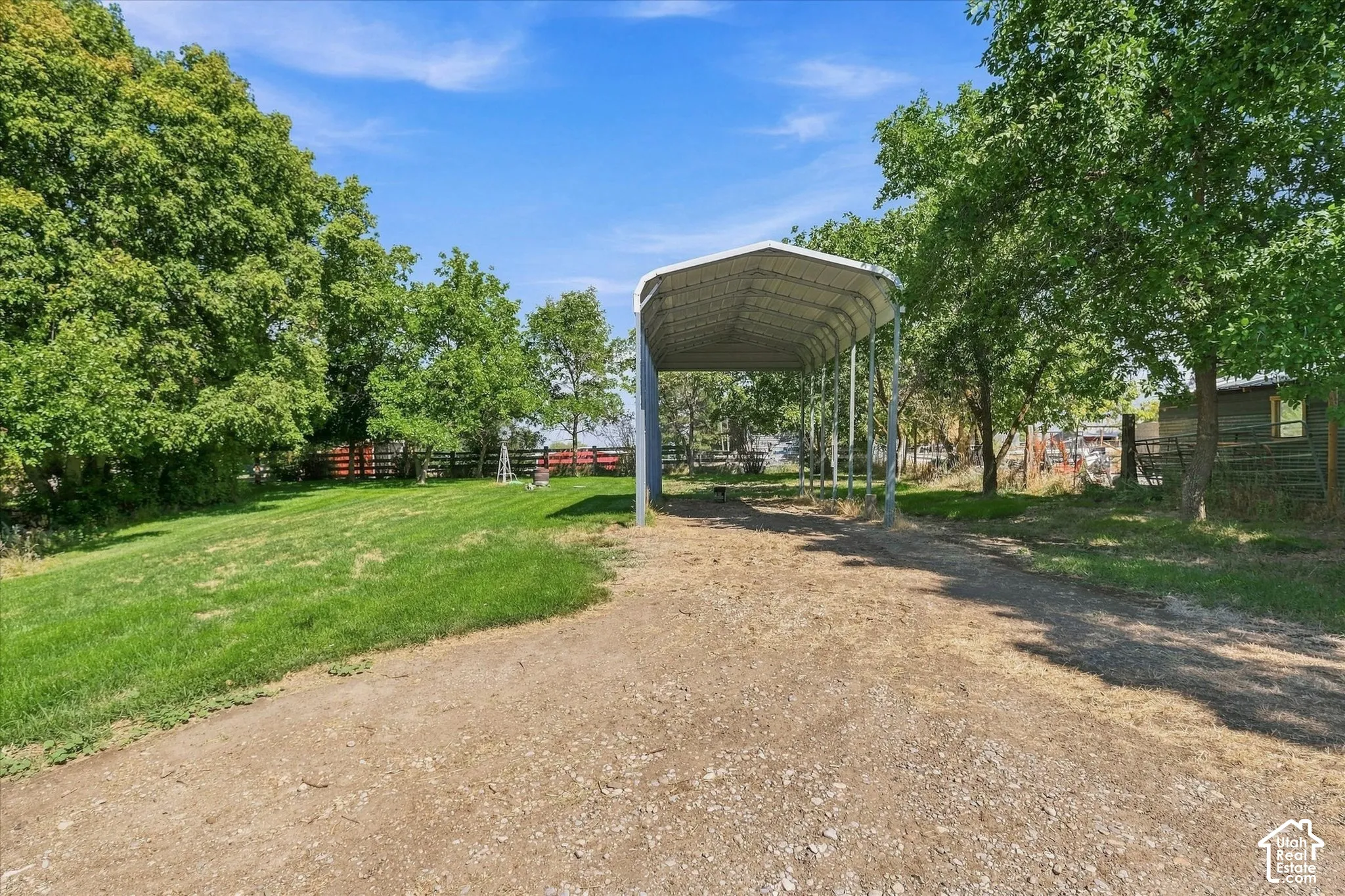 Expansive green lawn, mature trees, gravel driveway, and a large metal RV storage structure