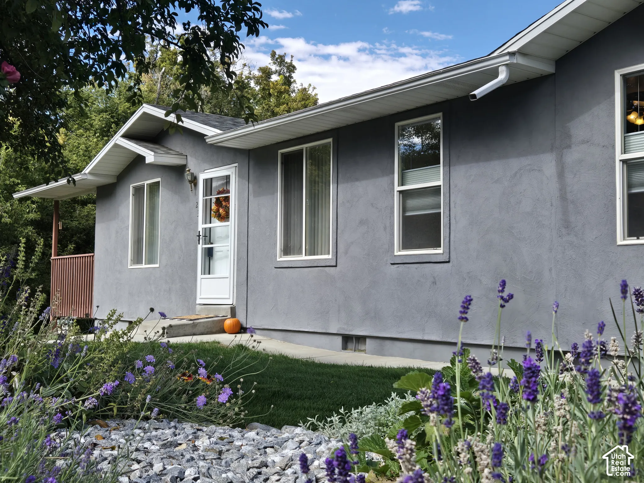Light gray stucco exterior with white-framed windows and lovely landscaping.