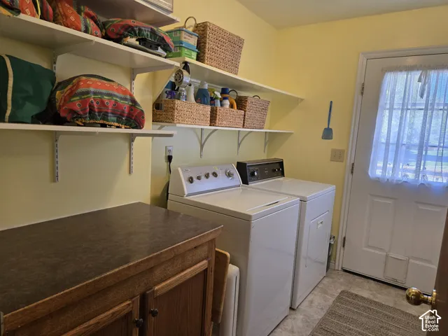 Integrated laundry appliances with durable flooring, open wall shelving, and a built-in wood-finish cabinet with a dark countertop leading to the back yard and ramp