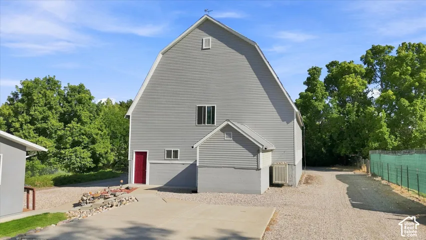 Gambrel roof structure with horizontal siding, a red entry door, and a gravel driveway. It's a great barn!