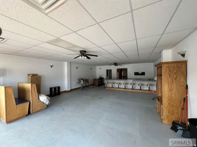 Spacious interior featuring a long bar with multiple stools, exposed concrete flooring, and ceiling fans