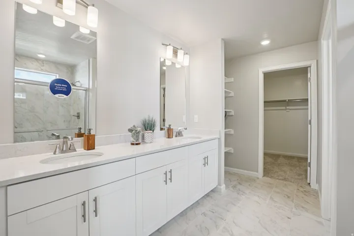 Double vanity with white cabinetry and brushed nickel hardware, expansive countertop space, integrated shower with glass enclosure, tiled flooring, and built-in shelving