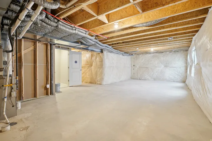 Unfinished basement with exposed wood joists and concrete flooring, featuring a partially framed wall and an interior door