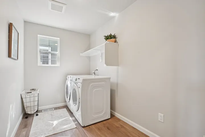 Dedicated laundry space featuring wood-finish flooring, a window with blinds, and white wall shelving