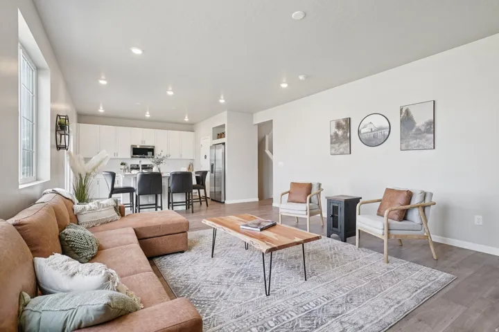 Open-concept living space with wood-finish flooring, recessed lighting, and a kitchen featuring white cabinetry, stainless steel appliances, and a breakfast bar