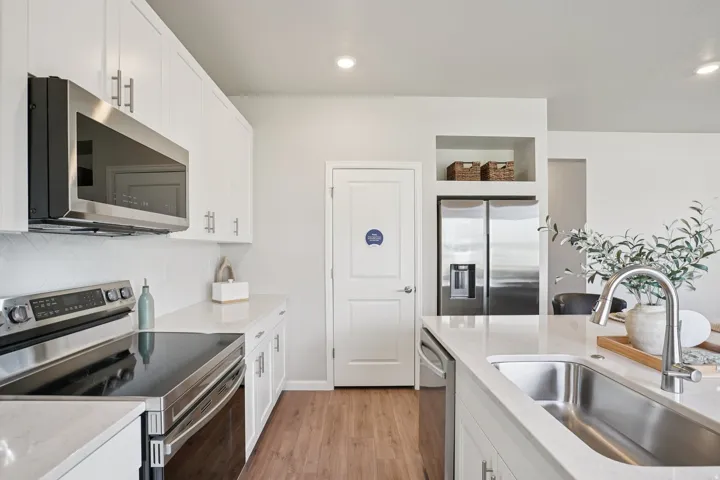 Kitchen featuring stainless steel appliances, white cabinetry, integrated sink, light-toned countertops, and wood-finish flooring