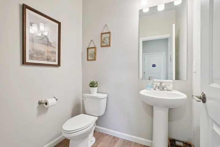 Pedestal sink with a coordinating wall-mounted mirror, white toilet, and wood-finish flooring