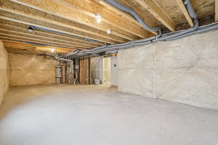 Unfinished basement featuring exposed wood joists, concrete flooring, and insulated perimeter walls