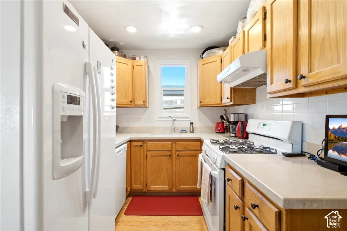 U-shaped kitchen with wood cabinetry, white tile backsplash, and light-toned countertops and appliances (all included).