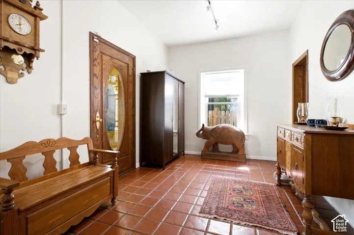 Terracotta tile flooring, recessed window, wood-finish paneled door with stained glass, track lighting, and a built-in cabinet in the main entry.