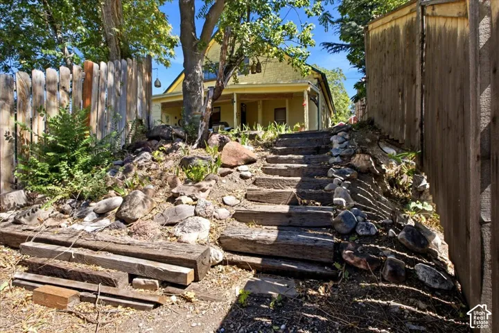Rear yard with tiered landscaping with wood timber steps, natural rock accents, and established trees