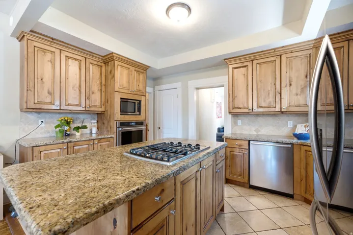 Kitchen featuring wood-finish cabinetry, granite countertops, a central island with a gas cooktop, built-in microwave and oven, and stainless steel appliances