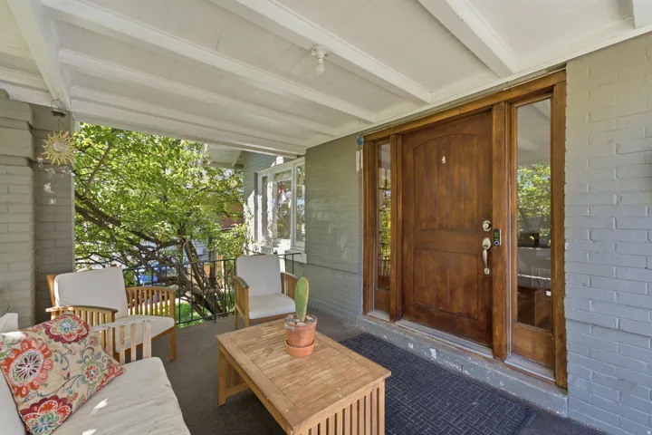 Covered porch with exposed wood beams, brick facade, and a paneled wood entry door with sidelights