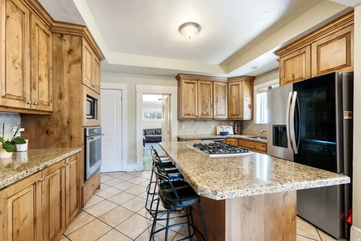 Kitchen with wood cabinetry, granite countertops, tile flooring, and stainless steel appliances including a built-in oven and microwave
