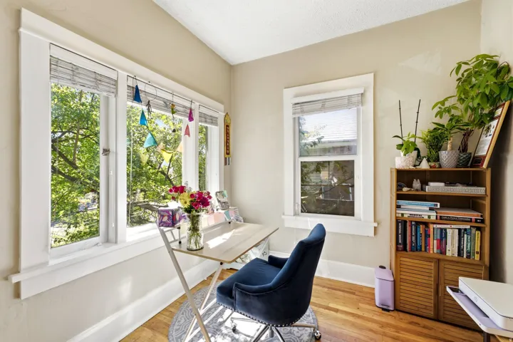 Multiple windows with white trim, wood-finish flooring, and a built-in wood-tone bookcase with louvered doors