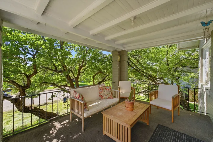 Covered porch with painted wood plank ceiling and exposed beams, featuring a dark wrought iron railing