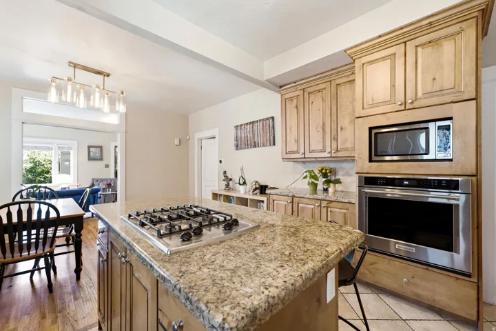Kitchen featuring light wood cabinetry, stone countertops, stainless steel built-in appliances, a gas cooktop on the island, and a tile floor