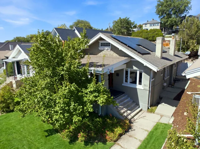 Gabled bungalow with solar panels, multiple chimneys, and a front yard with mature landscaping