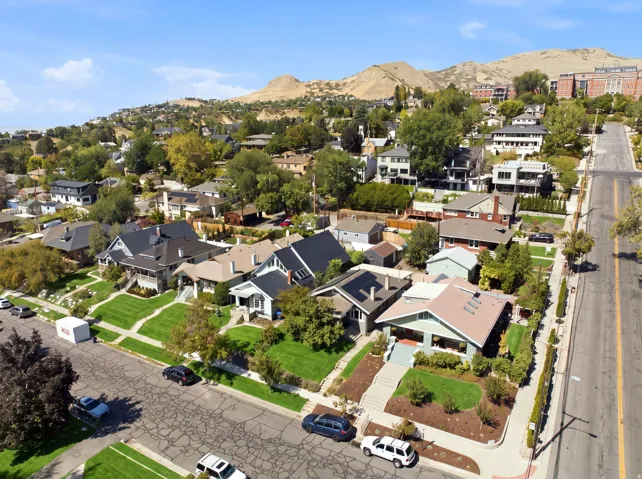 Residential street with sidewalks and mature trees, set against a backdrop of distant hills