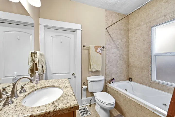 Built-in soaking tub with tiled surround, dual-pane window, and tiled shower walls