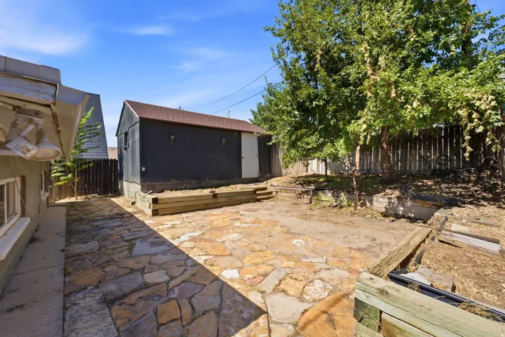Expansive outdoor space featuring a flagstone patio, mature trees, and a detached structure with a pitched roof