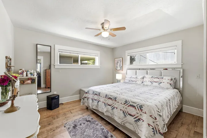 Wood-finish flooring with light gray walls, two windows, and a ceiling fan