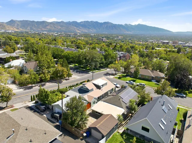 Residential neighborhood with mature trees, mountain backdrop, and multiple properties featuring pitched roofs and solar panels
