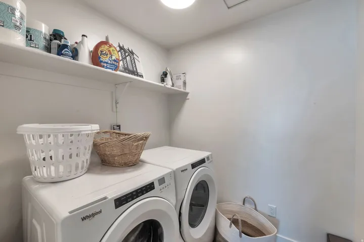 Stacked washer and dryer unit with Whirlpool appliances, overhead built-in shelving, and recessed lighting