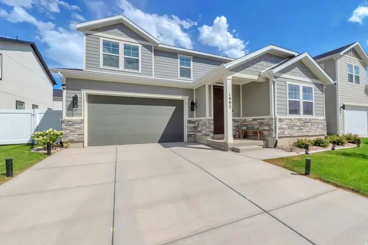 Two-story residence featuring a covered entry, stone veneer accents, an attached garage, and a concrete driveway