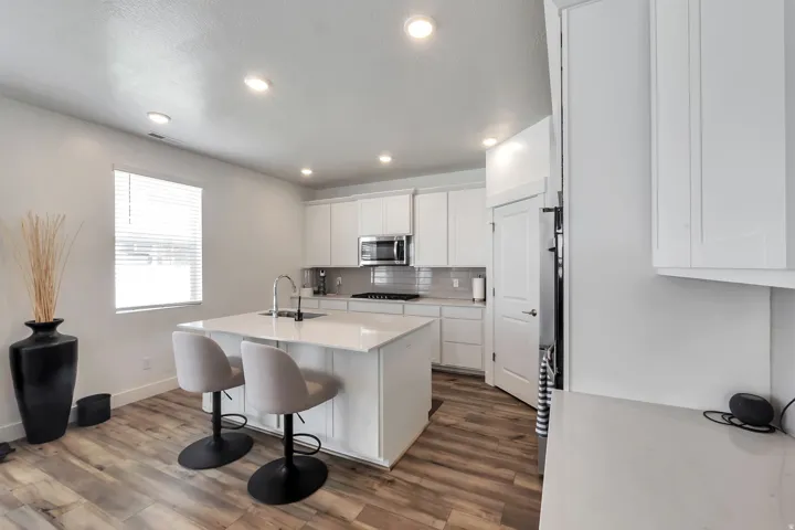 Kitchen featuring recessed lighting, a central island with a sink, white cabinetry, stainless steel appliances, and wood-finish flooring