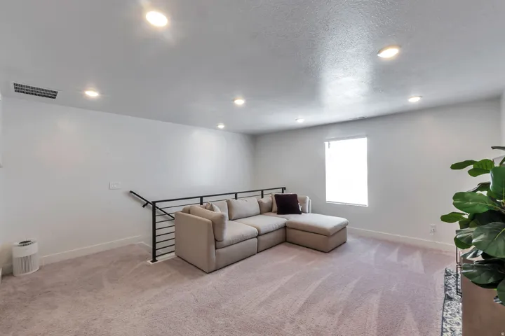 Recessed lighting illuminates a carpeted room with light-toned walls and a window featuring blinds