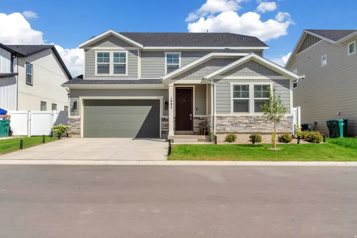 Two-story residence featuring a gray exterior siding, stone accents, a two-car garage, a dark entry door, and a concrete driveway