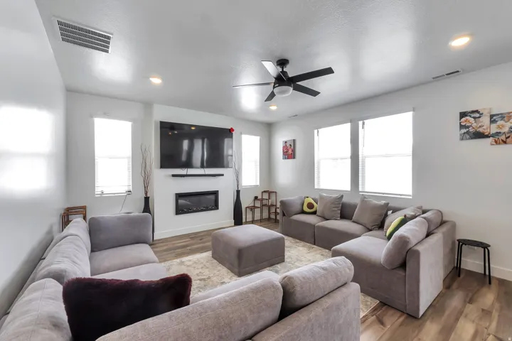 Integrated wall-mounted fireplace with mantel, ceiling fan with light fixture, recessed lighting, and wood-finish flooring