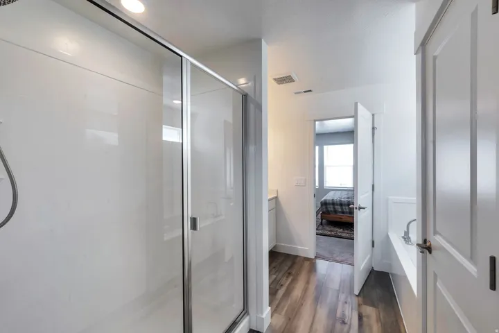 White shower enclosure with glass sliding door, wood-finish flooring, and white panel doors