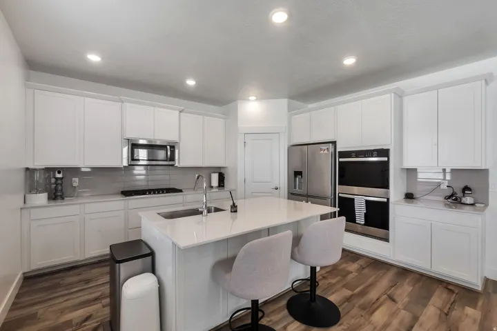 White cabinetry, light countertops, wood-finish flooring, stainless steel appliances, and recessed lighting