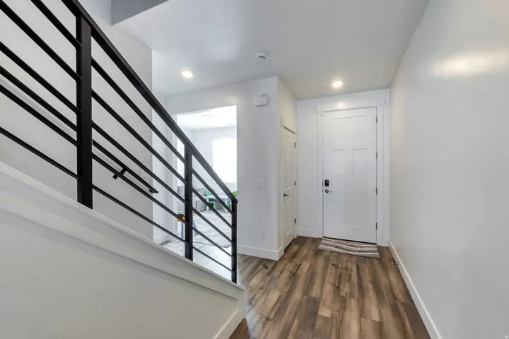 Contemporary metal stair railing, recessed ceiling lighting, wood-finish flooring, and a white paneled entry door with smart lock hardware
