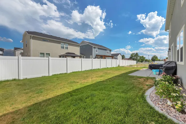 Expansive rear yard featuring a concrete patio, white privacy fencing, and landscaping with decorative rock and plantings