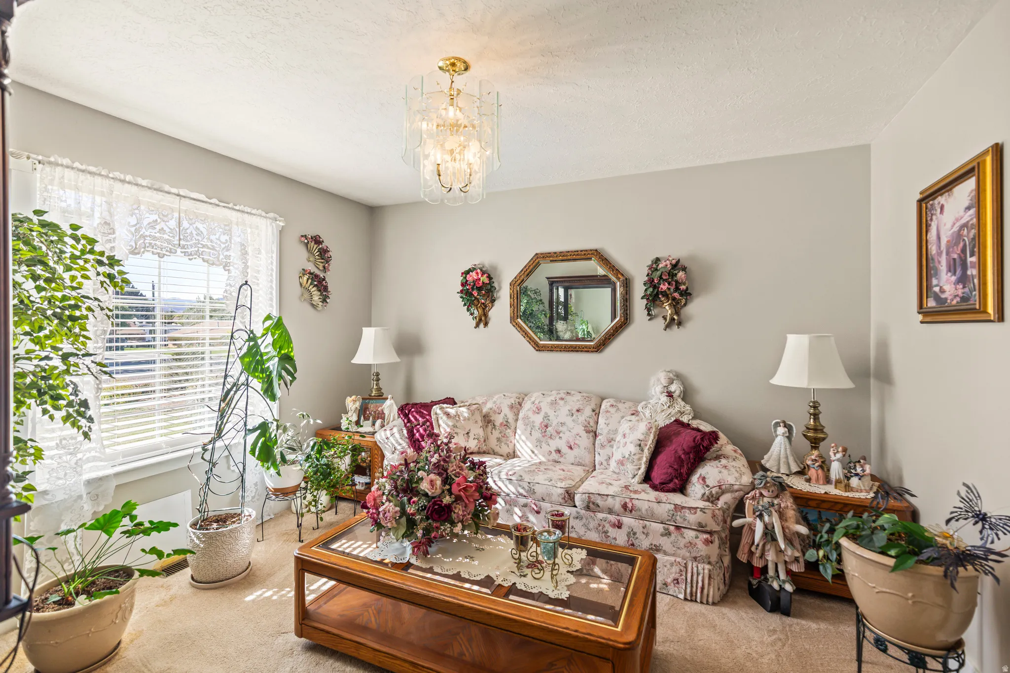 Ceiling-mounted chandelier, window with horizontal blinds, carpeted flooring, and light-toned wall paint