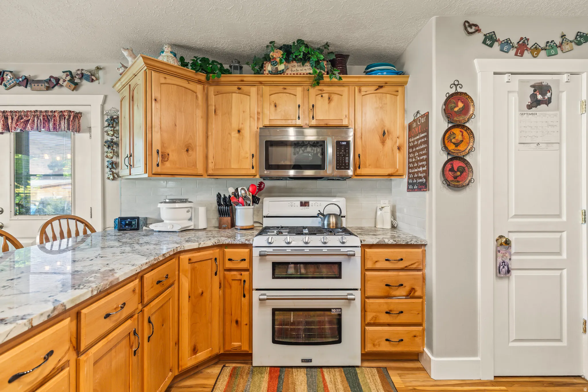 Kitchen featuring wood cabinetry, light-toned countertops, a stainless steel microwave, and a white double oven range