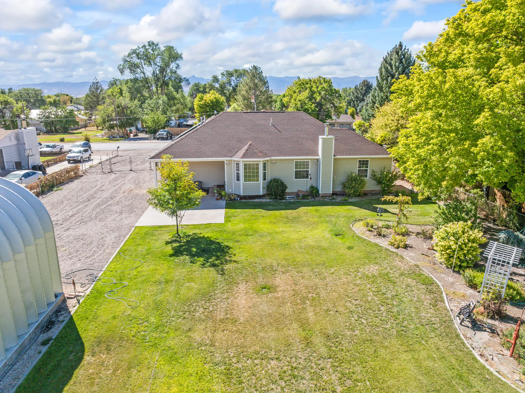 Expansive green lawn with established landscaping, mature trees, and a concrete patio