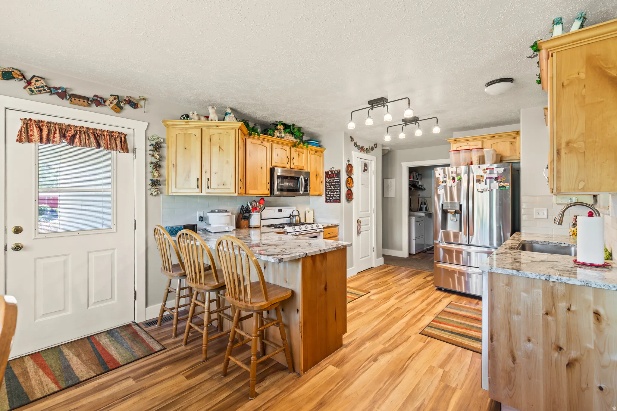 Wood-finish flooring, light wood cabinetry, stainless steel appliances, granite countertops, and a kitchen island with seating