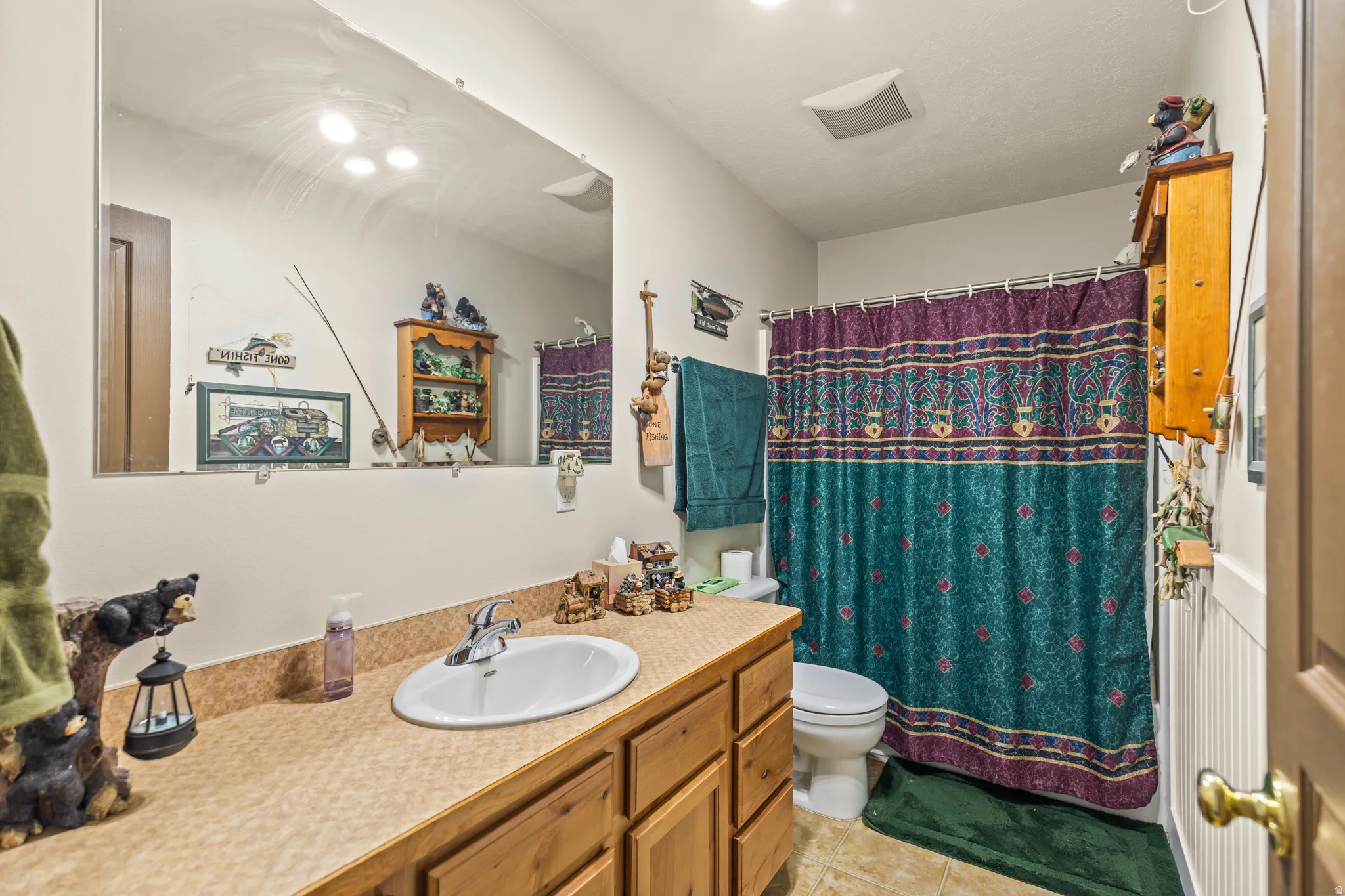 Vanity with integrated sink, wood-finish cabinetry, neutral countertop, and large wall-mounted mirror