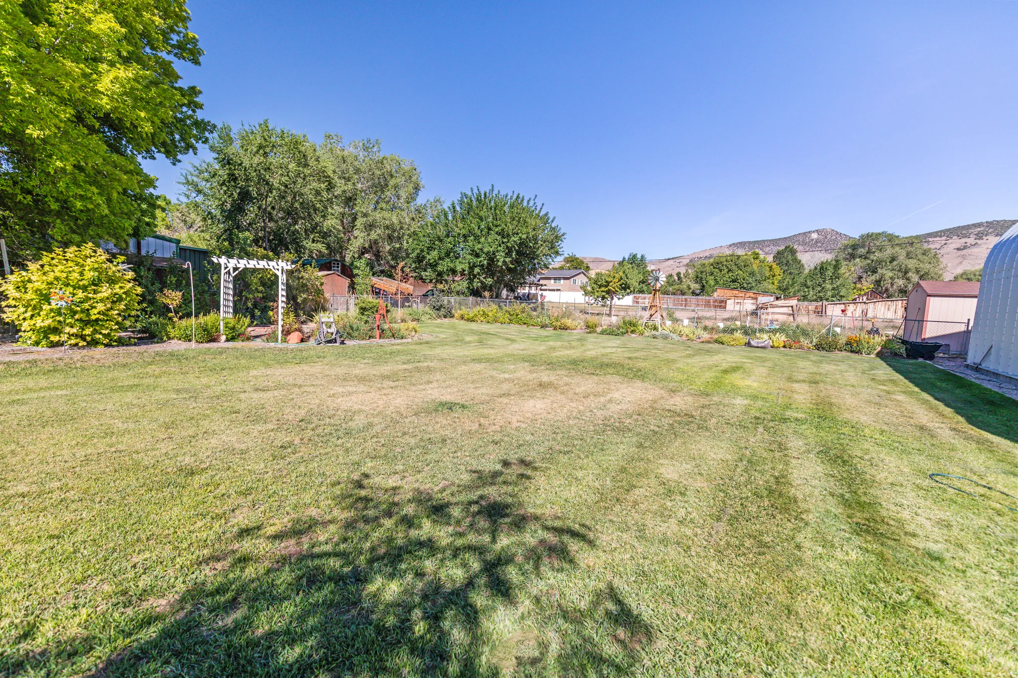 Expansive lawn area with mature trees, garden beds, and a decorative arbor