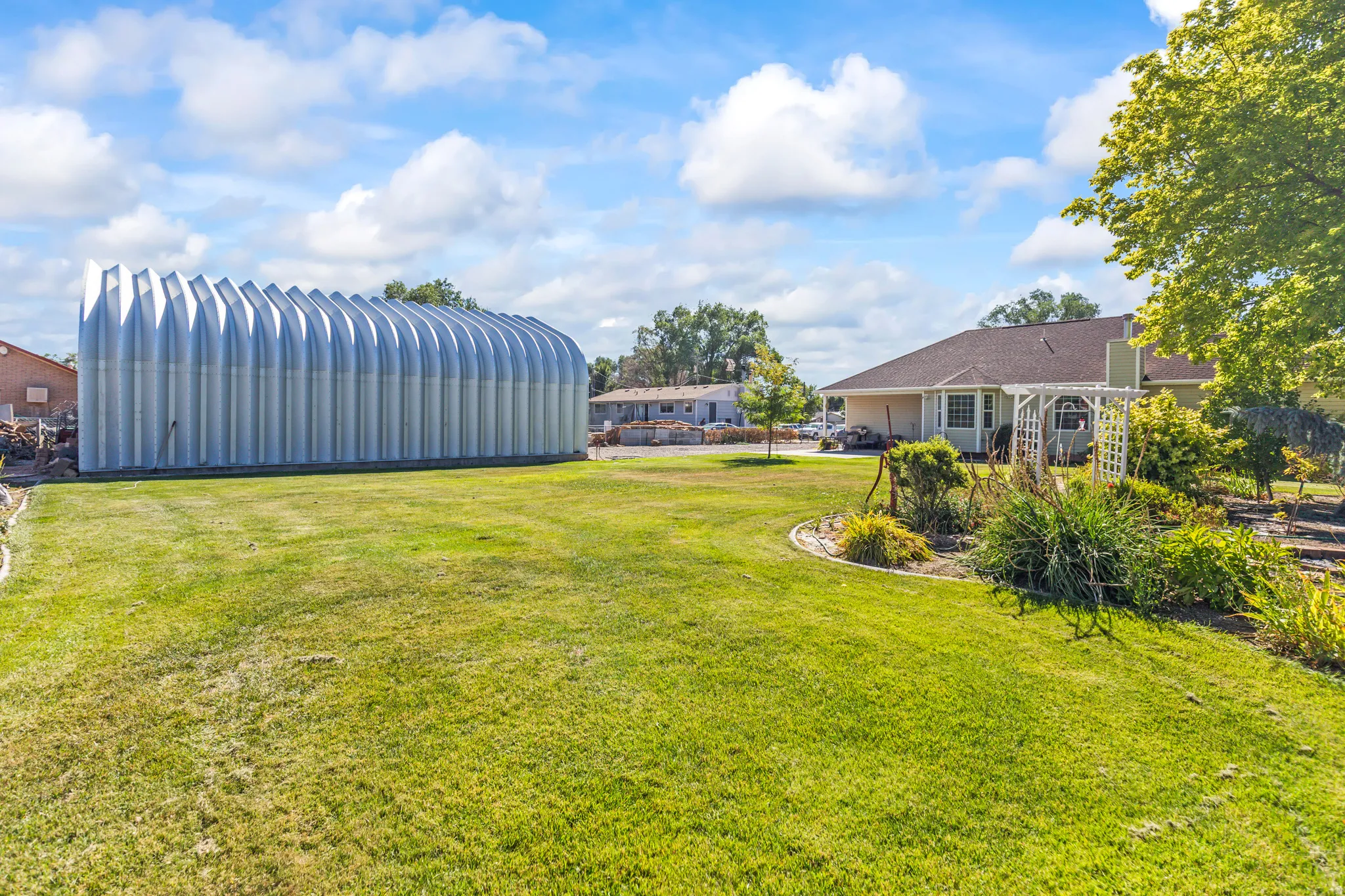 Expansive grassy area featuring a large arched metal outbuilding and a landscaped garden bed