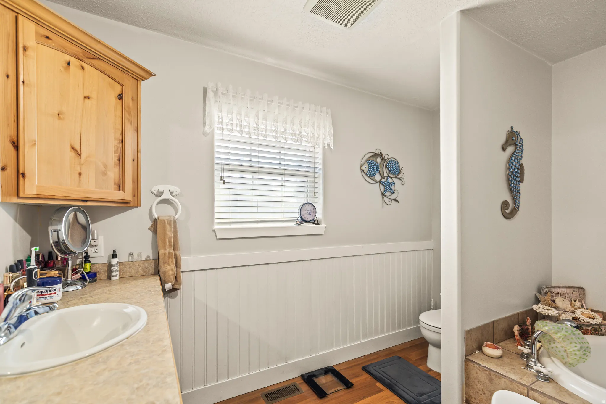 Vanity with an integrated sink, wood-finish upper cabinetry, and a window with blinds
