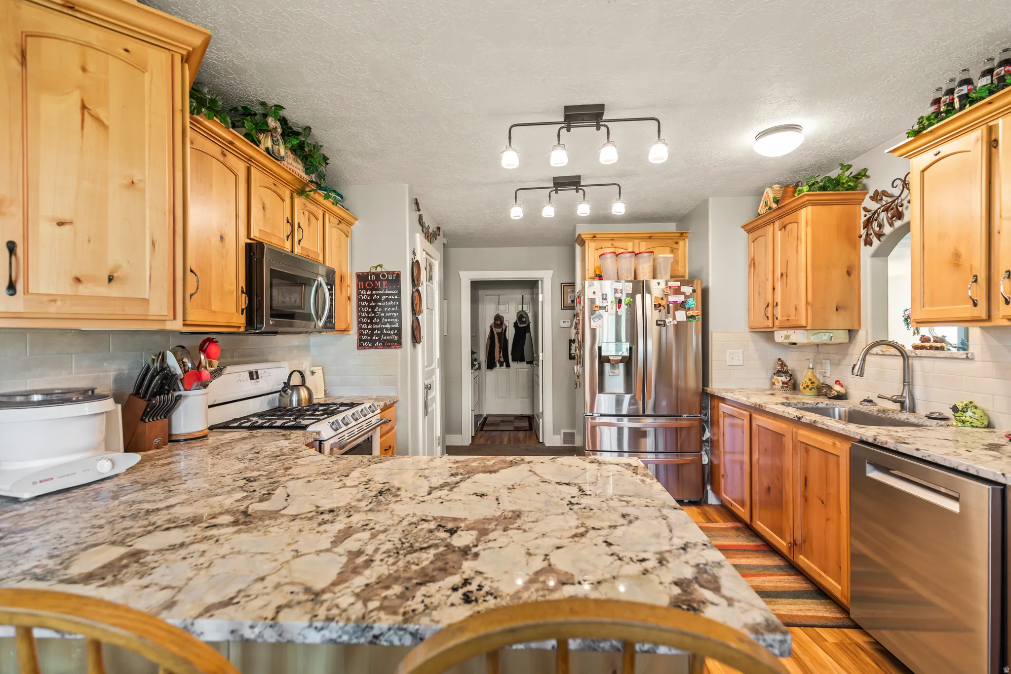 Kitchen featuring light wood cabinetry, stainless steel appliances, granite countertops, and a subway tile backsplash